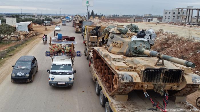 Flüchtende aus Idlib mit vollbepackten Autos auf der einen Seite, türkische Militärfahrzeuge auf der anderen
