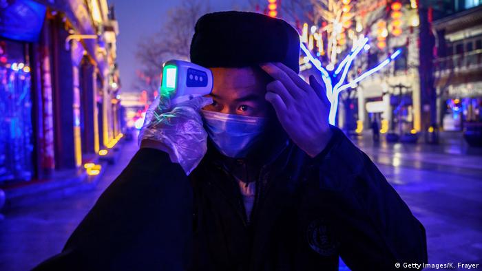 A Chinese worker wears a protective mask as he has his temperature checked in a nearly empty and shuttered commercial street on February 12, 2020 in Beijing, China. 