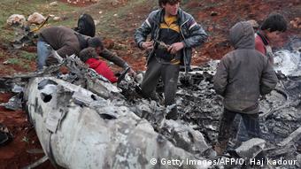 Sírios inspecionam destroços de um helicóptero militar do governo após ele ter sido abatido sobre a província de Aleppo