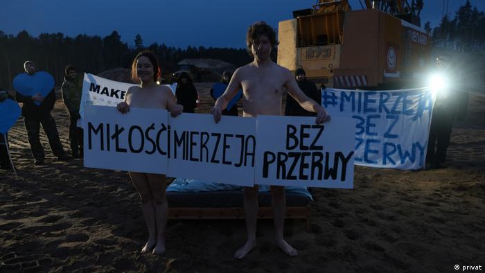 Naked protesters hold banners in front of their bodies 
