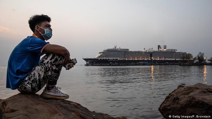 A Cambodian man sits by the ocean at sunset near the MS Westerdam cruise ship docked nearby in Sihanoukville, Cambodia on February 17, 2020