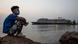 A Cambodian man sits by the ocean at sunset near the MS Westerdam cruise ship docked nearby in Sihanoukville, Cambodia on February 17, 2020 A Cambodian man sits by the ocean at sunset near the MS Westerdam cruise ship docked nearby in Sihanoukville, Cambodia on February 17, 2020