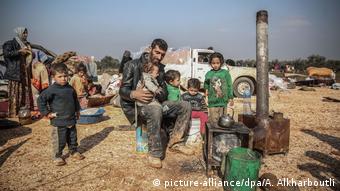 Homem está sentado com seus filhos na frente de um forno em um acampamento improvisado em Idlib