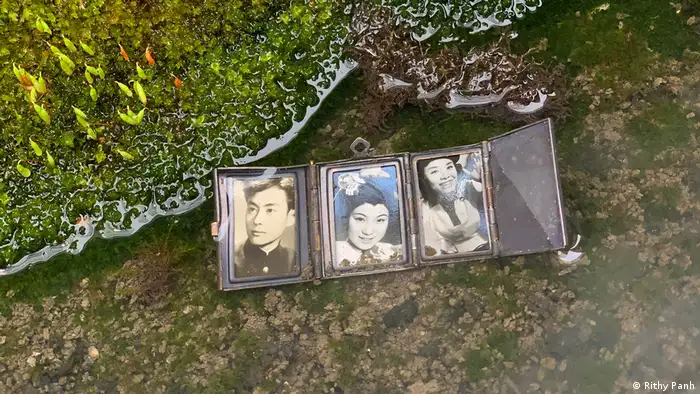 Ein Teich, in dem ein Faltbuch mit drei Schwarzweiß-Fotografien liegt (Rithy Panh)