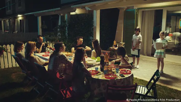 Acht Personen am Tisch auf einer Terrasse, zwei Kinder tragen etwas vor (Pepito Produzioni/Amka Film Production)