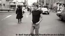 Black and white photo of a young man in jeans and a t-shirt crossing a city street: Untitled 22 from the Christopher Street series, 1976 (Sunil Gupta/Hales Gallery/Barbican Art Gallery)