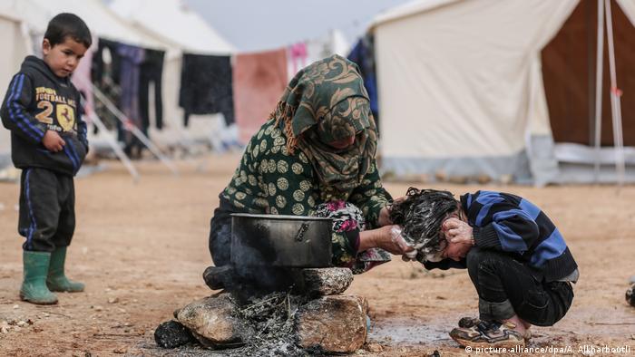 A woman washes the hair of a child in Syria while another child looks on
