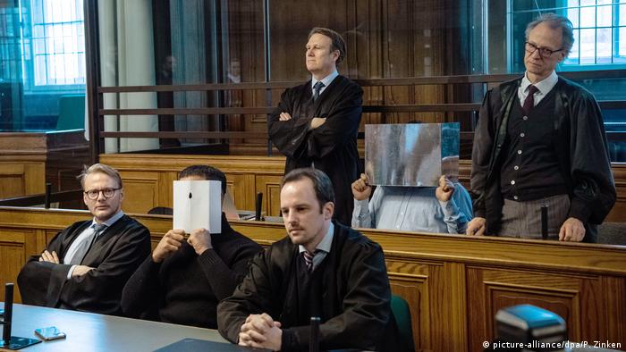 Two accused hiding their faces while sitting in the courtroom with their lawyers