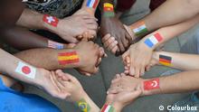Menschen mit aufgemalten Länderfahnen auf den Armen reichen sich die Hände 