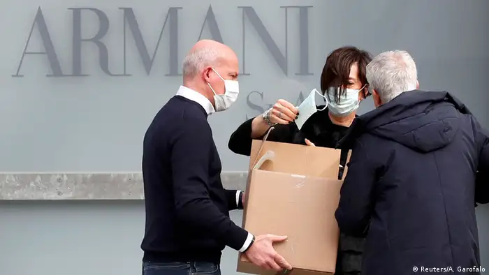 Drei Personen mit einem Karton voller Gesichtsmasken vor dem Schriftzug Armani (Reuters/A. Garofalo)