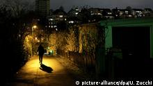 Eine Person hastet in der Dunkelheit unter dem Schein einer Strassenlaterne entlang. | Verwendung weltweit