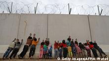 Displaced Syrian children stand by the Turkish border wall at an informal camp in Kafr Lusin village in Syria's northwestern province of Idlib, on February 21, 2020. - Six months ago, the family fled deadly fighting in Idlib province of northwest Syria, seeking shelter near the border village of Kafr Lusin, where dozens of families live in an informal camp for the displaced. Turkey, which already hosts the world's largest number of Syrian refugees with around 3.6 million people, has placed barbed wire and watchtowers along the wall to prevent any more crossings. (Photo by AAREF WATAD / AFP) (Photo by AAREF WATAD/AFP via Getty Images)