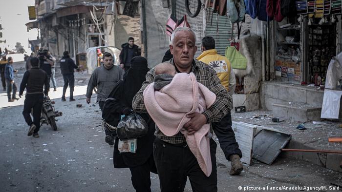 Man carries a baby amid damaged buildings in Idlib