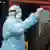 Мужчина в защитном костюме и респираторной маске измеряет пассажиру с азиатской внешностью темпратуру в московском общественном транспорте