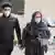 Мужчина с женщиной в масках идут по улице Тегерана