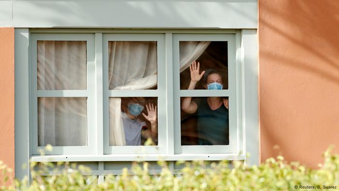 Gente con máscaras de respiración mirando a través de una ventana y saludando. 