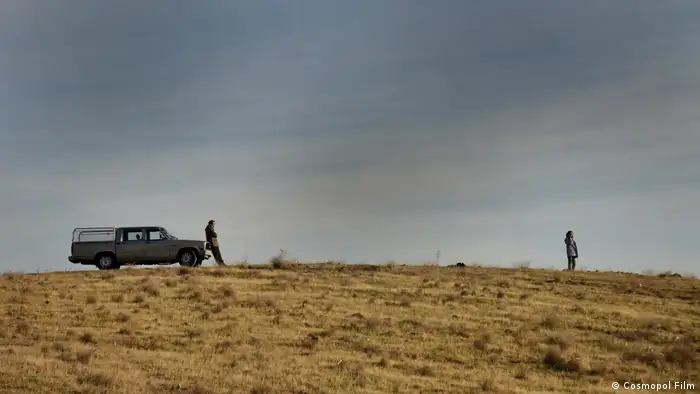 Zwei Menschen, von Weitem gesehen, stehen auf einem Hügel, eine Person lehnt an einem Pickup-Truck (Cosmopol Film)