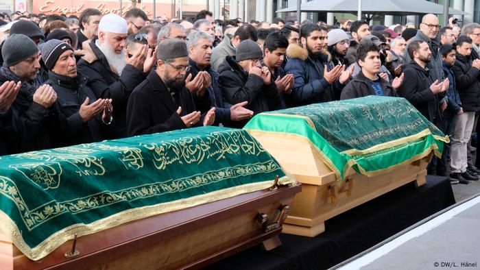 Betende Muslime hinter Särgen, die mit Tüchern mit arabischen Schriftzeichen bedeckt sind