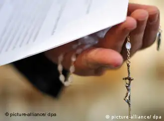 A priest's hand holds a rosary beneath some papers
