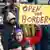 Entre outros manifestantes, mulher levanta cartaz que diz: "Abram as fronteiras"