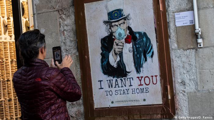 Eine Frau in Barcelona fotografiert ein Poster des Künstlers TVBoy mit der Aufschrift I want you to stay home am 13. März 2020