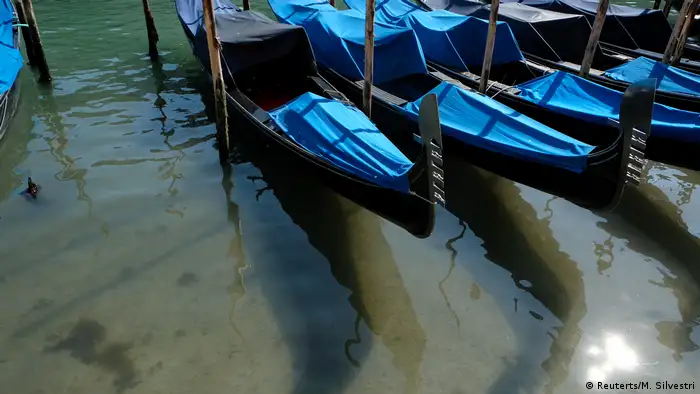 An Wasserpfählen festgemachte Gondeln liegen auf dem klaren Wasser eines der beliebten Kanäle Venedigs