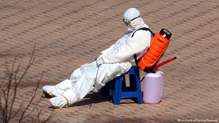 An exhausted quarantine worker carrying a disinfectant keg on his shoulders takes a brief break after disinfecting ambulances