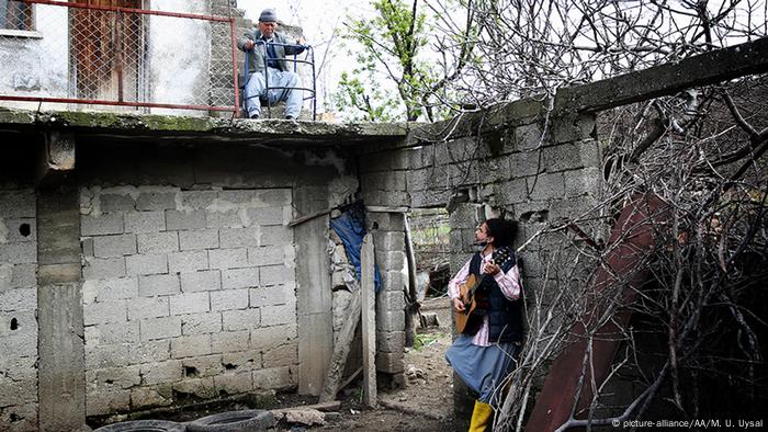 Ein Mann mit Gitarre steht in einem Innenhof und sieht zu einem älteren Mann auf einem Balkon herauf (picture-alliance/AA/M. U. Uysal)
