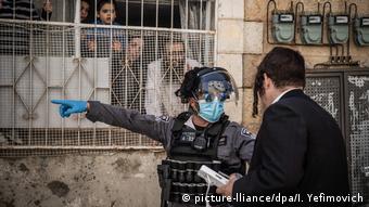 in israelischer Polizist, der Mundschutz und Einweg-Handschuhe trägt, weist einen ultra-orthodoxen Juden im Viertel Mea Shearim an, nach Hause zu gehen.