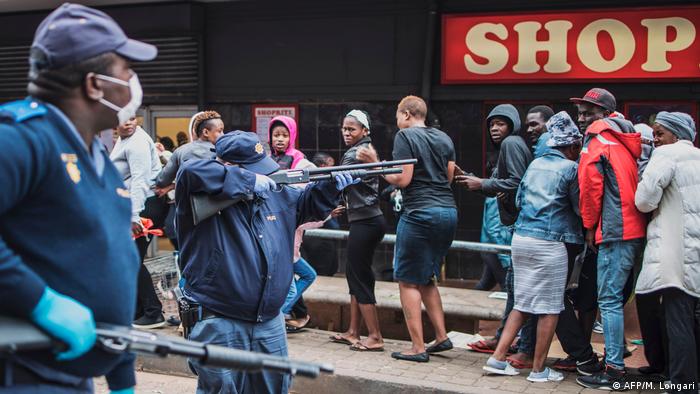 Polícia aponta arma a populares para manterem a distância de segurança no bairro de Yeoville, em Joanesburgo