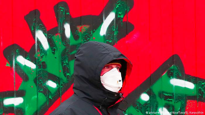 Мужчина в защитной маске на фоне граффити с изображением коронавируса