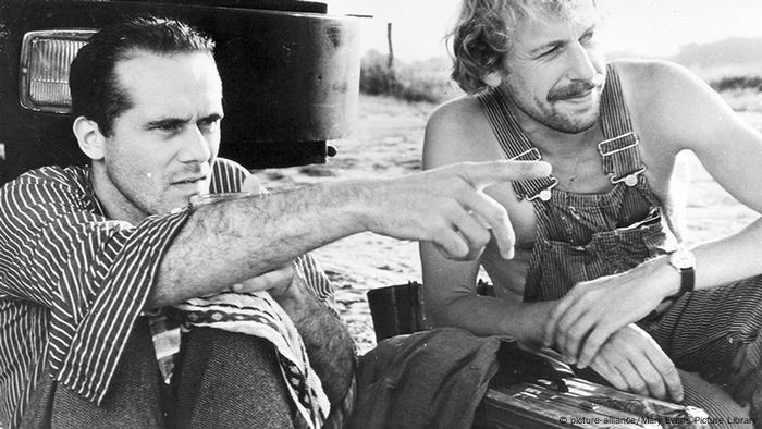 Filmszene aus Im Lauf der Zeit: Zwei Männer im Gespräch in Arbeitskluft, der eine Mann deutet auf ein Ziel, im Hintergrund ist ein Teil eines Lkws zu sehen (Bild: picture-alliance/Mary Evans Picture Library)