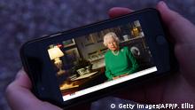 A picture shows a person in Birkenhead, northwest England on April 5, 2020 posing holding a smartphone showing Britain's Queen Elizabeth II deliver a special address to the UK and Commonwealth recorded at Windsor Castle in relation to the coronavirus outbreak. - Queen Elizabeth II urgeed people to rise to the challenge posed by the coronavirus outbreak, in a rare special address to Britain and Commonwealth nations on Sunday. (Photo by Paul ELLIS / AFP) (Photo by PAUL ELLIS/AFP via Getty Images)
