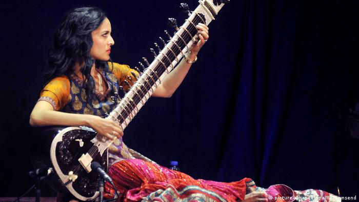 Woman with black hair in a colorful dress plays the sitar