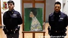 This image taken from a video distributed Wednesday, Dec. 11, 2019 by Italian police shows two police officers standing next to painting which was found inside a gallery's walls, in Piacenza, northern Italy. A gardener at the Ricci Oddi modern art gallery in the northern city of Piacenza told Italian state TV on Tuesday that he was clearing ivy from the gallery's walls when he noticed a metal panel in which he found a bag inside a space within the walls. When the bag was opened it contained a painting that might be Klimt's “Portrait of a Lady,” which disappeared from the gallery during renovations in February 1997. (Italian Police via AP) |