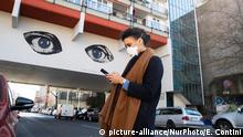 01.04.2020 *** A young woman wearing a protective mask looks at her smartphone while passing by a grafitti representing two big watching eyes in Berlin, Germany on April 1, 2020. Illustrative Editorial (Photo by Emmanuele Contini/NurPhoto) | Keine Weitergabe an Wiederverkäufer.