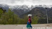 07.04.2020, Indien, Dharmsala: Schneebedeckte Gipfel des Dhauladhar-Gebirges, einem Teil der kleineren Himalaya-Gebirgskette, sind im Hintergrund klar zu sehen, als eine Frau ihre Einkäufe aus einem Laden trägt. Foto: Ashwini Bhatia/AP/dpa +++ dpa-Bildfunk +++ |
