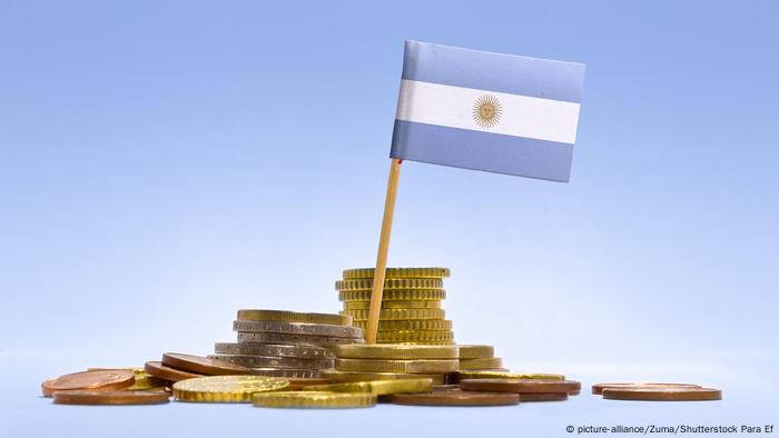 La bandera argentina, sobre monedas doradas y de cobre, símbolo de la deuda argentina.