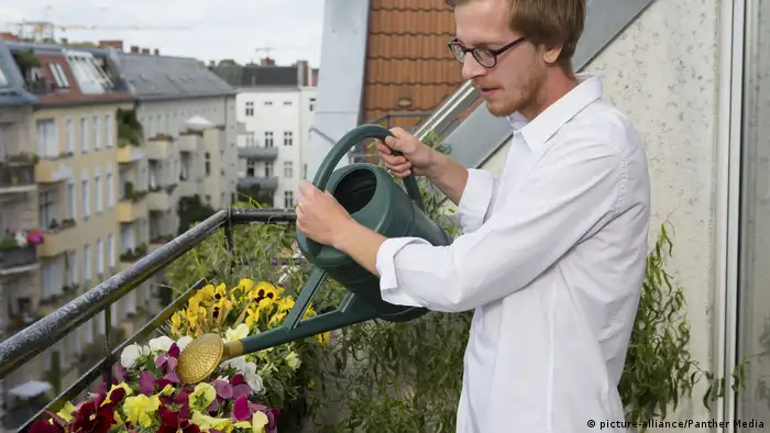 A man waters flowers on his balcony with a watering can
