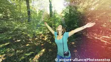A woman walks in the woods with her arms outstretched