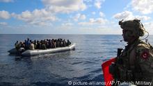 In this image provided by the Turkish Military, a member of Turkish forces, right, on a boat approaches migrants aboard a dinghy in the mid Mediterranean Sea, Wednesday, Jan. 29, 2020. The military said that a military ship, TCG Gaziantep, assisted the migrants and provided medical aid before handing them over to the Libyan Coast Guard. The frigate is in the region to support NATO's Mediterranean Shield Operation and to assist NATO's Marine Guard Operation. (Turkish Military via AP)