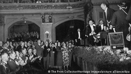 Links uniformierte Parteimitglieder, die applaudieren. Rechts auf der Bühne verbeugt sich Wilhelm Furtwängler.