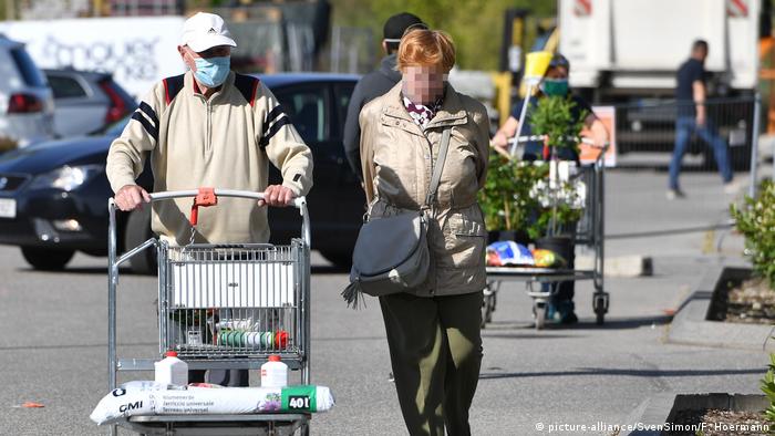 A man and a woman leave a store, with only the man wearing a face mask