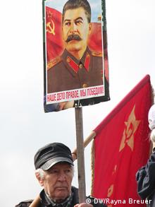 Ein älterer Mann präsentiert ein Schild mit Stalins Porträt vor dem Denkmal der roten Armee in Sofia in die Höhe