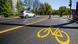 A image of a road with a temporary cycle path and an image of a bike painted in yellow. A image of a road with a temporary cycle path and an image of a bike painted in yellow.