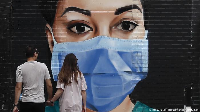A masked NHS worker painted on a mural looks on as a couple walks past in London.