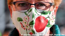 Maskenpflicht in Bayern in allen Geschaeften und im oeffentlichen Personennahverkehr.
Masken in allen Variationen gehoeren mittlerweile zum Alltag in Zeiten von Corona.
Eine selbstgenaehte,wiederverwendbare Mundschutzmaske,Mundschutz,Mund-Nasen Schutz einer Frau zeigt florale Muster und eine rote Kirsche. | Verwendung weltweit