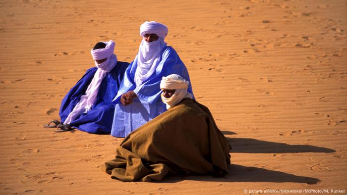Three Tuareg sit on the sand in long robes with headdresses and face veils (picture-alliance / blickwinkel / McPhoto / M. Runkel)