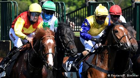 Jockeys reiten dicht nebeneinander bei einem Pferderennen aus der Startbox heraus. 