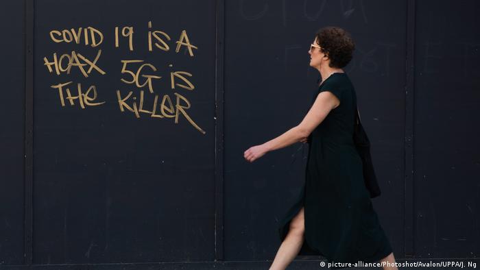 A woman walks past graffiti stating COVID-19 is a hoax 5G is the killer in London